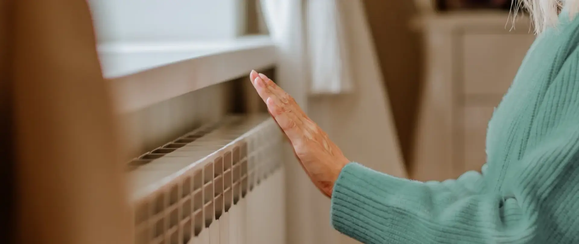 Eine Frau wärmt sich die Hand an der Heizung in einem gemütlichen Wohnzimmer