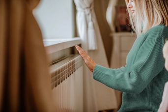 Eine Frau wärmt sich die Hand an der Heizung in einem gemütlichen Wohnzimmer