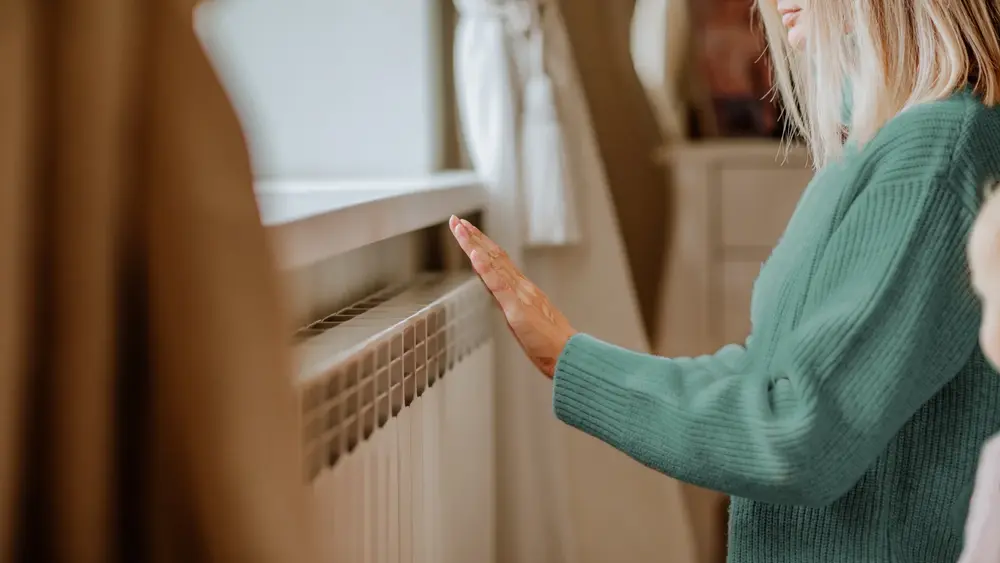 Eine Frau wärmt sich die Hand an der Heizung in einem gemütlichen Wohnzimmer