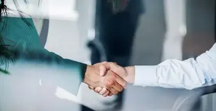 Jobs bei Westfalen Weser. Zwei Menschen schütteln sich die Hände. Das Foto wurde durch eine Glasscheibe geschossen. Ausschnitt der Arme.