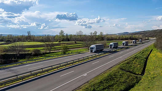 Effiziente Ladelösungen für elektrische LKW‑Fernstrecken Mehrere LKW fahren hintereinander über eine Autobahn in ländlicher Umgebung.