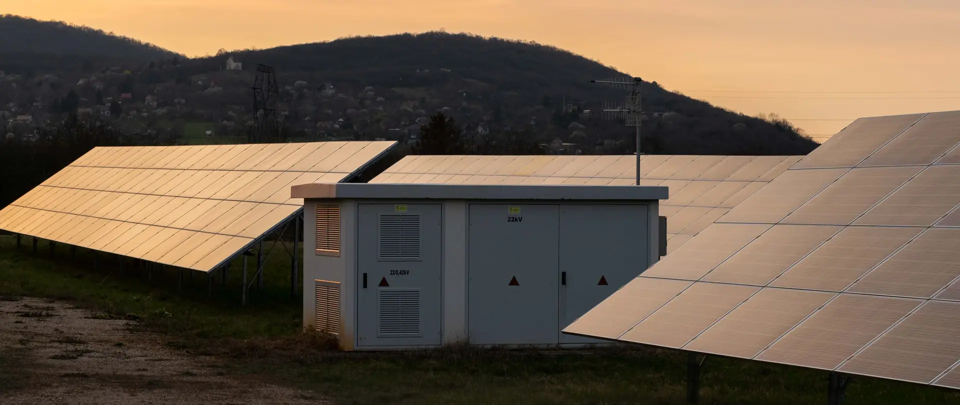 Eine Trafostation steht in einem Feld umgeben von Photovoltaikanlagen.