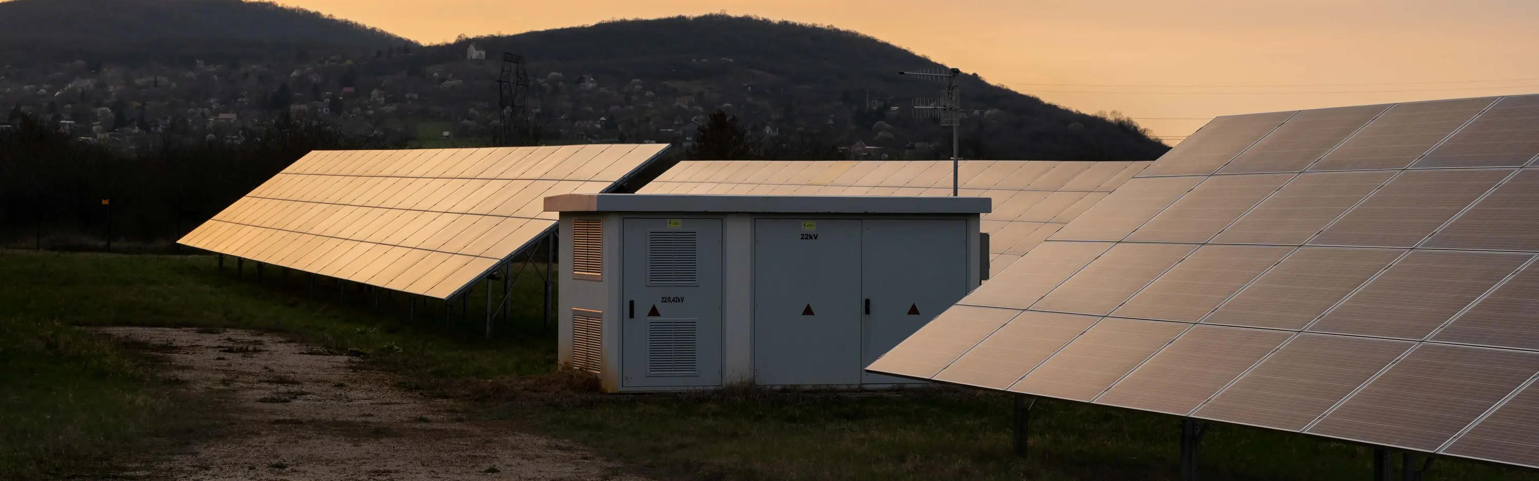 Eine Trafostation steht in einem Feld umgeben von Photovoltaikanlagen.