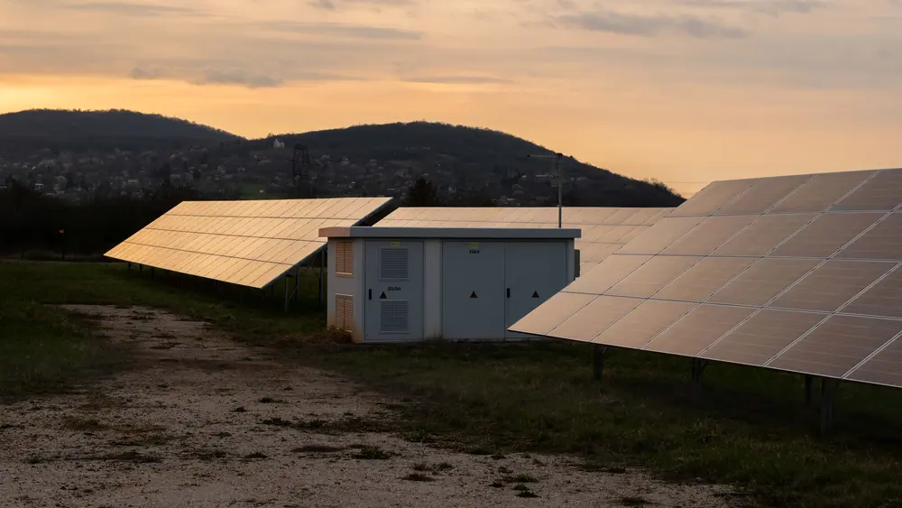 Eine Trafostation steht in einem Feld umgeben von Photovoltaikanlagen.