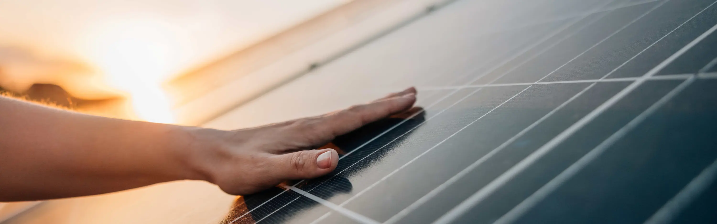 Eine Mann liegt flach auf einem Photovoltaikmodul während im Hintergrund die Sonne untergeht.