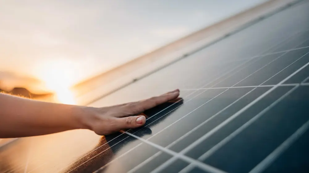 Eine Mann liegt flach auf einem Photovoltaikmodul während im Hintergrund die Sonne untergeht.