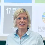 Eine lächelnde Frau mit kurzen blonden Haaren und einer blauen Bluse.