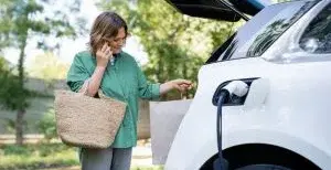 Eine Frau lädt über eine Schnellladesäulen ihr E-Auto während eines Einkaufs auf. Sie holt gerade etwas aus dem Kofferraum.