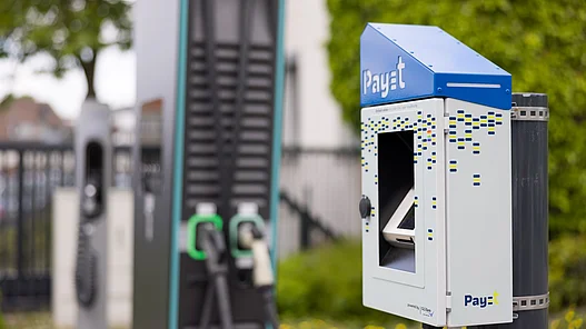 Eine Terminal mit integriertem Bezahlsystem steht neben einer Elektroauto Ladestation im Außenbereich.