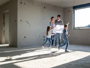 Eine Familie steht im Rohbau. Die Kinder spielen und die Eltern halten einen Plan in den Händen