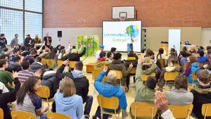 Schüler sitzen im Publikum, viele melden sich, während ein Referent zum Thema Energie spricht.