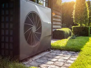 Eine Wärmepumpe steht im grünen Garten. Die Sonne scheint zum Abend.