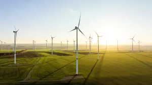 Mehrere Windräder stehen auf einem weiten, grünen Feld und erzeugen erneuerbare Energie bei Sonnenaufgang.