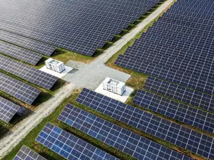 Solarpark mit netzdienlichen Batteriespeichern Eine große Solaranlage mit Batteriespeichern und Schotterweg verläuft durch grüne Flächen mit Solarpaneelen.