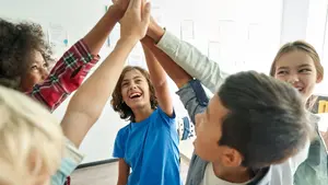 Kinder stehen im Kreis und geben sich in einem Klassenraum gemeinsam ein Gruppen-High-Five.