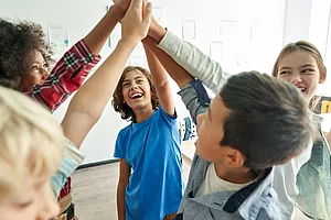 Teamwork und Gemeinschaft erleben Kinder stehen im Kreis und geben sich in einem Klassenraum gemeinsam ein Gruppen-High-Five.