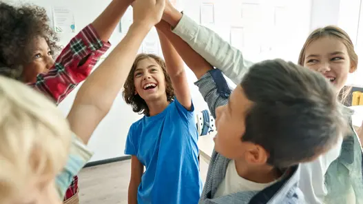 Teamwork und Gemeinschaft erleben Kinder stehen im Kreis und geben sich in einem Klassenraum gemeinsam ein Gruppen-High-Five.