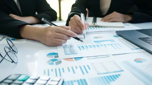 Zwei Personen analysieren Diagramme und Tabellen zu Energiespeichern in einem Besprechungsraum mit Laptop und Unterlagen.