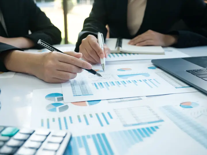 Zwei Personen analysieren Diagramme und Tabellen zu Energiespeichern in einem Besprechungsraum mit Laptop und Unterlagen.