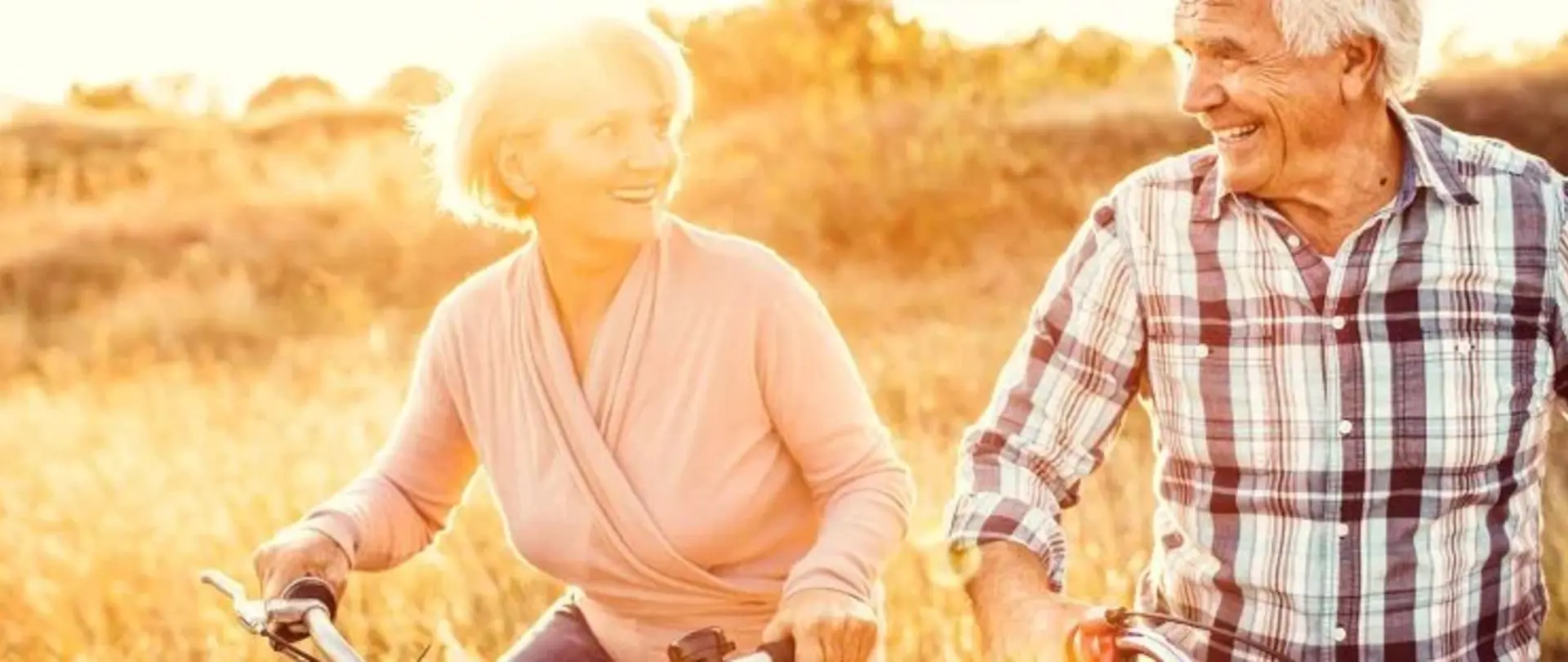 Zwei Rentner fahren in der Natur Fahrrad und gucken sich glücklich an.