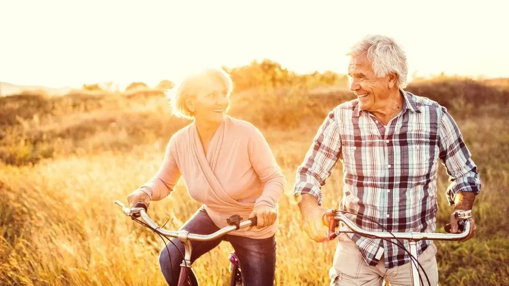 Zwei Rentner fahren in der Natur Fahrrad und gucken sich glücklich an.