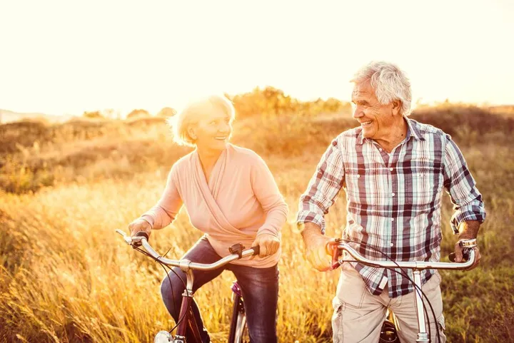 Zwei Rentner fahren in der Natur Fahrrad und gucken sich glücklich an.