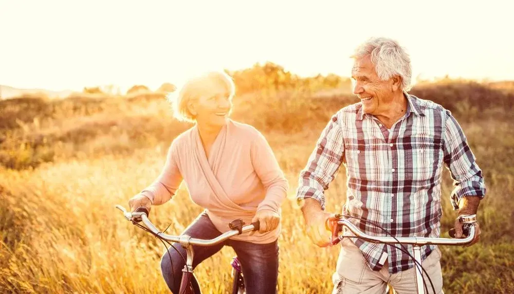 Zwei Rentner fahren in der Natur Fahrrad und gucken sich glücklich an.