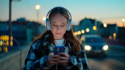 Mädchen schaut aufs Handy und geht eine Straße entlang