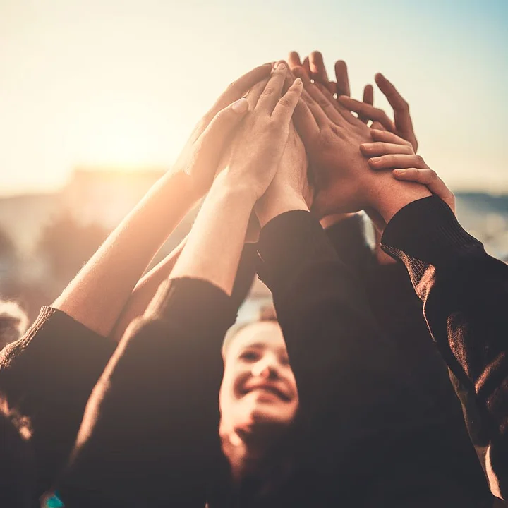 Man sieht eine Gruppe Menschen im Sonnenlicht, die ihre Hände zusammen klatschen. Ein Gesicht ist unscharf zu erkennen