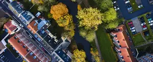 Aus Vogelperspektive sieht man ein Wohngebiet mit mehreren Wohnhäusern, Fahrzeugen und einem Fluss. Das Wohngebiet befindet sich im Grünen mit vielen Bäumen
