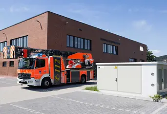 Eine Trafostation steht vor dem Gebäude der Feuerwehr in Holzminden und im Hintergrund ist ebenfalls ein Feuerwehrauto geparkt.