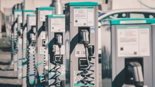 Eine Reihe von Ladesäulen mit Kabeln und Infotafeln bietet Ladeinfrastruktur für mehrere Elektrofahrzeuge gleichzeitig.