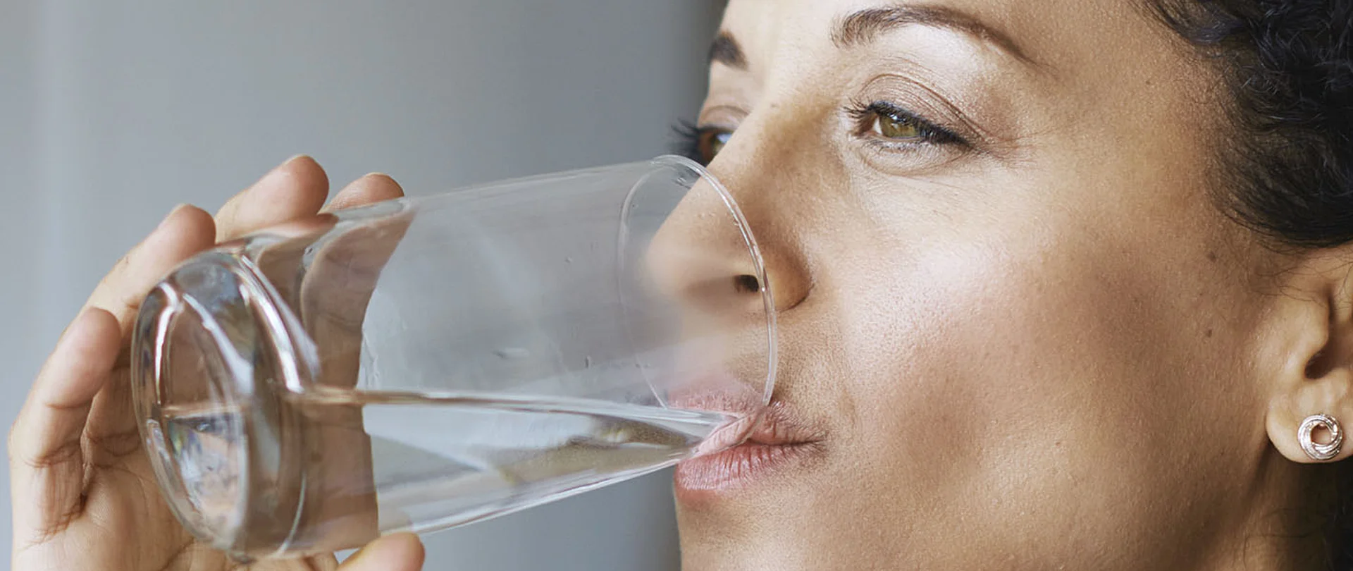 Nahaufnahme einer Frau, die genussvoll aus einem Glas Wasser trinkt.