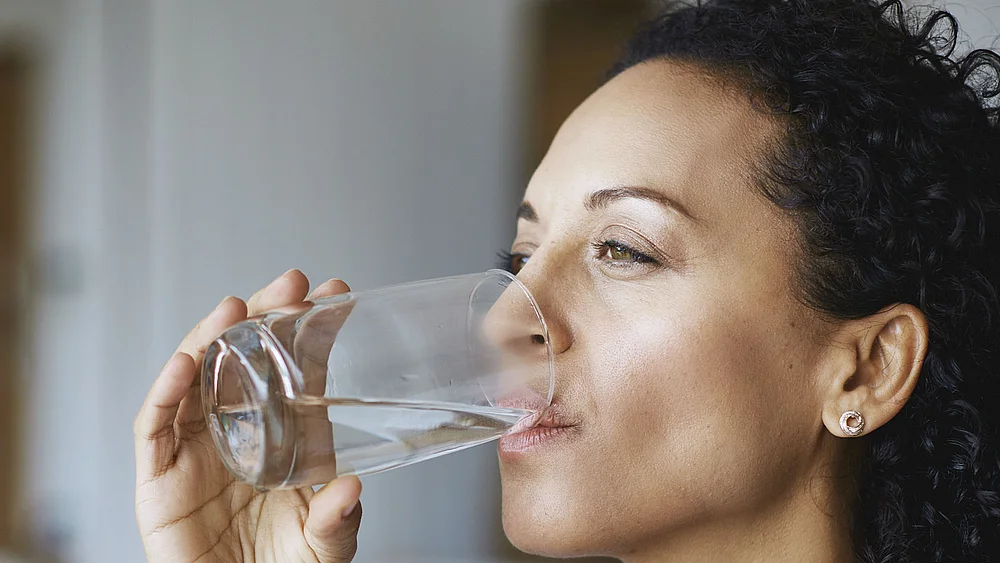Nahaufnahme einer Frau, die genussvoll aus einem Glas Wasser trinkt.