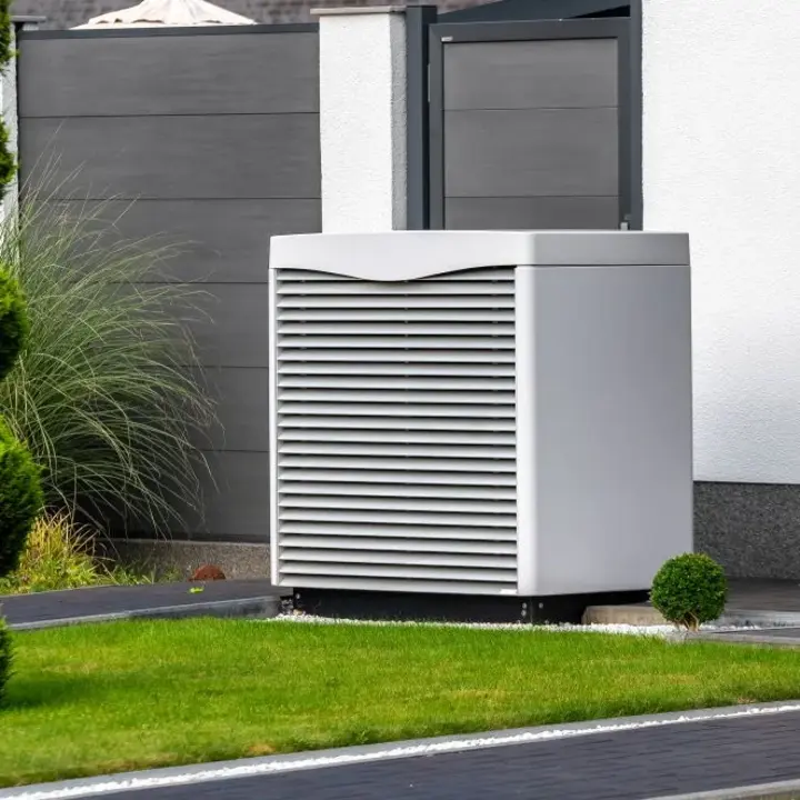 Eine weiße Wärmepumpe steht im Garten an der Hauswand