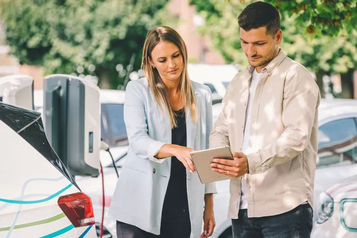 Frau und Mann stehen vor einer Wallbox und einem Elektroauto