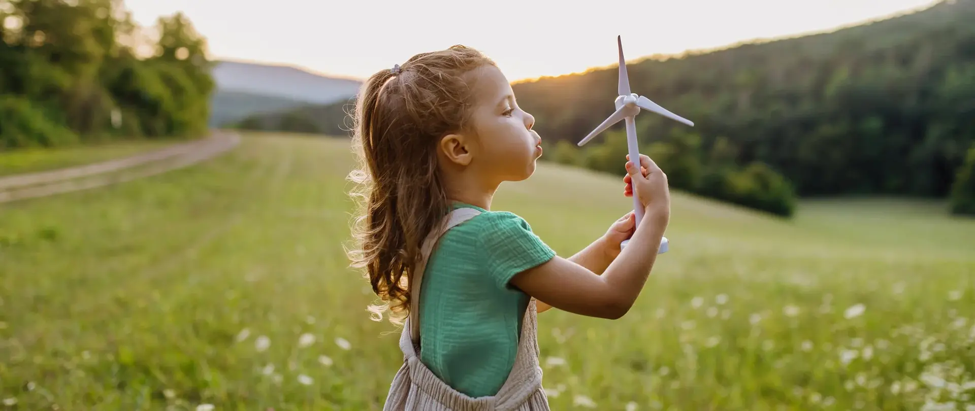 Kleines Mädchen auf der Wiese hält ein Windradmodell in den Händen.