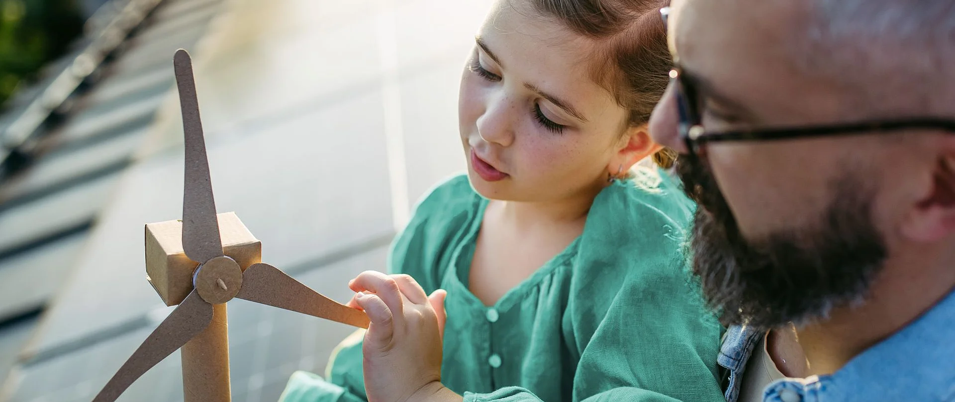 Vater und Tochter sitzen auf einem PV Dach und betrachten ein kleiner Windrad