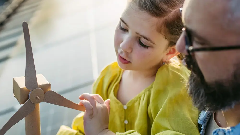 Vater und Tochter sitzen auf einem PV Dach und betrachten ein kleiner Windrad