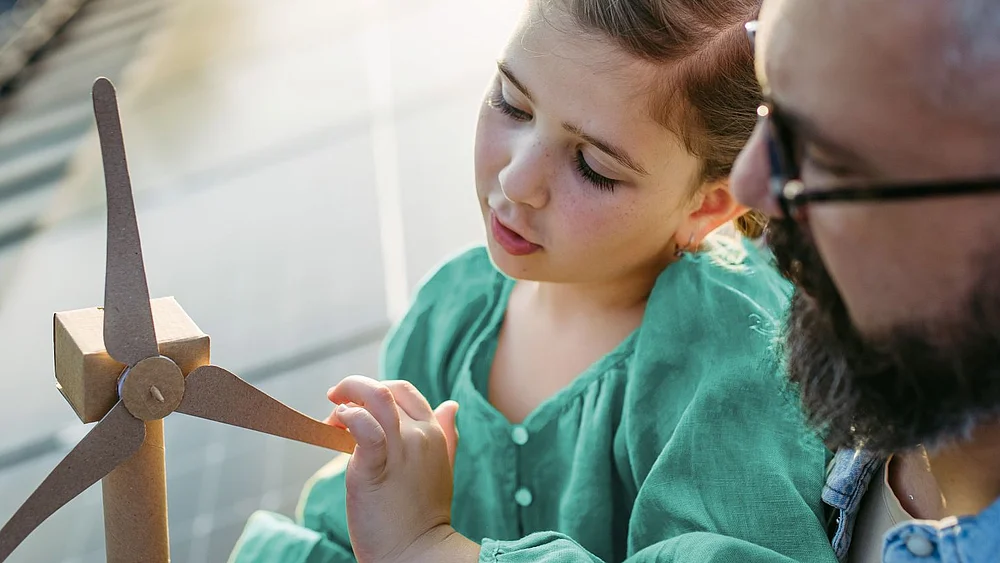 Vater und Tochter sitzen auf einem PV Dach und betrachten ein kleiner Windrad