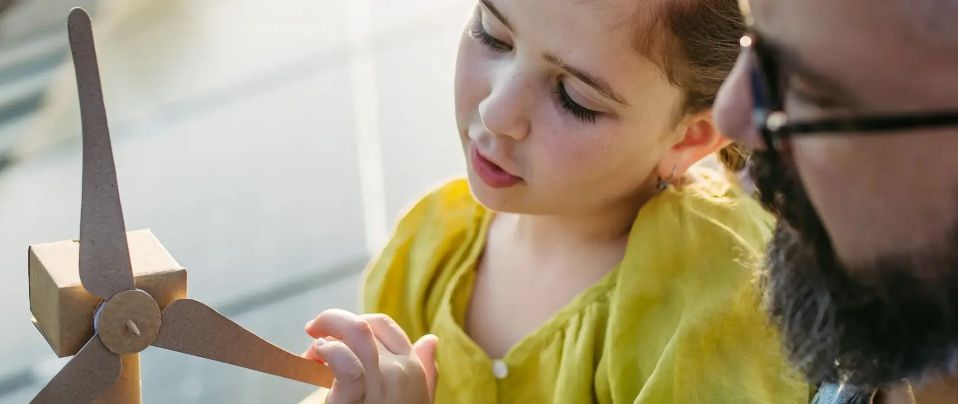 Vater und Tochter sitzen auf einem PV Dach und betrachten ein kleiner Windrad