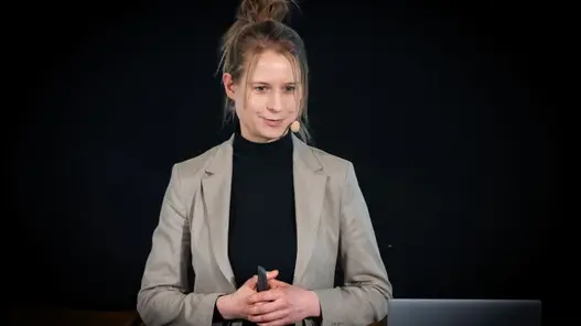 Westfalen Weser Forum 2026 Rednerin Man sieht eine junge Frau im grauen Blazer. Sie hält eine Rede vor schwarzem Hintergrund.