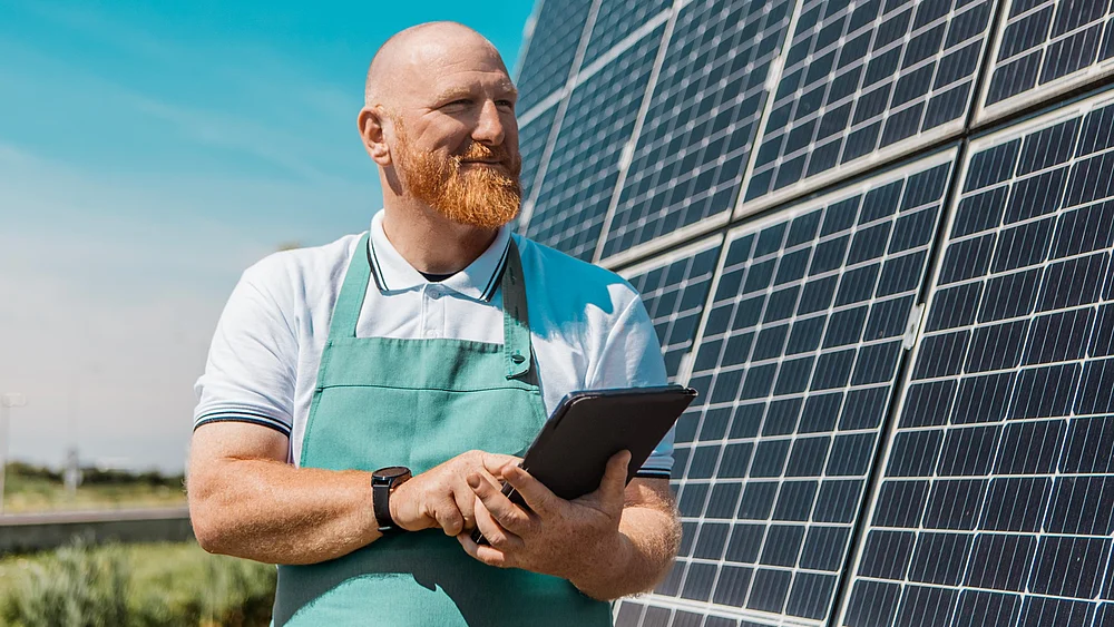 Ein Mann mit Schürze steht vor einer großen PV-Anlage und hält ein Klemmbrett in der Hand.