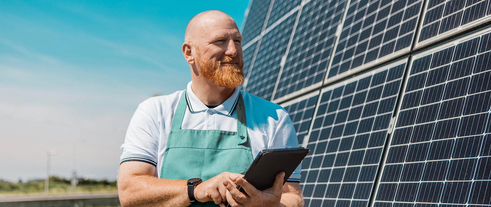 Ein Mann mit Schürze steht vor einer großen PV-Anlage und hält ein Klemmbrett in der Hand.
