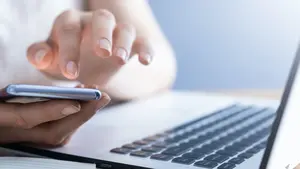 Mensch tipp auf einem Handy am Laptop.