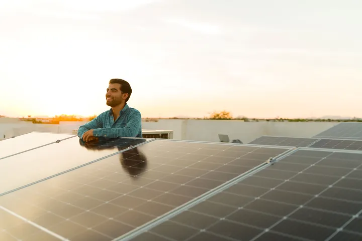 Ein Mann steht bei einem Sonnenuntergang hinter einer PV-Freiflächenanlage und schaut in die Ferne.