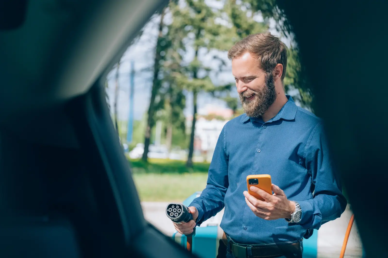 Eine Person lädt ihr Elektroauto und hält ein Ladekabel von einer Schnellladesäule und ein Handy in der Hand.