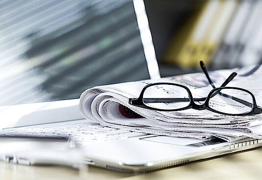 Eine Brille liegt auf einer Zeitung mit Laptop