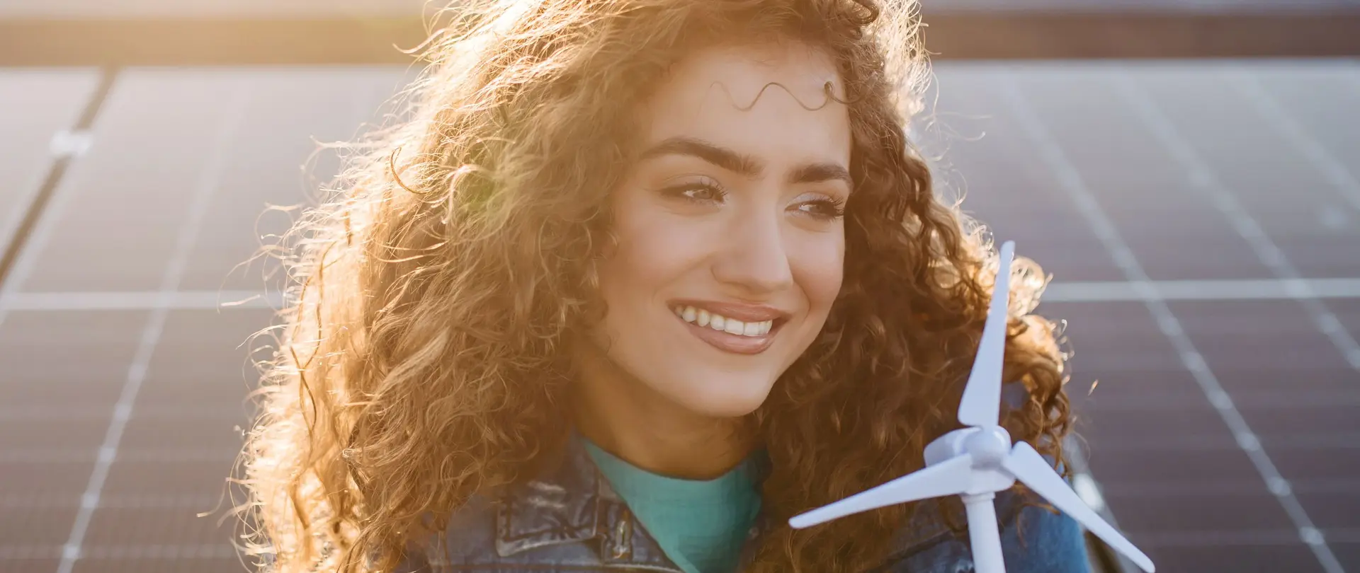 Eine Person hält ein Windturbinenmodell vor Solarpaneelen und symbolisiert nachhaltige Energieerzeugung.