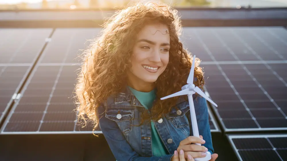Eine Person hält ein Windturbinenmodell vor Solarpaneelen und symbolisiert nachhaltige Energieerzeugung.